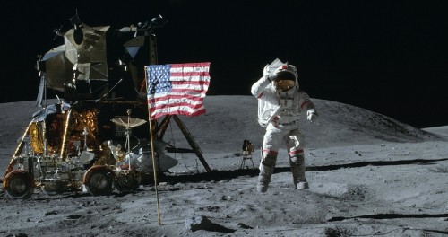 John Young von der Apollo 16 Mission salutiert springend neben der US-Flaggs